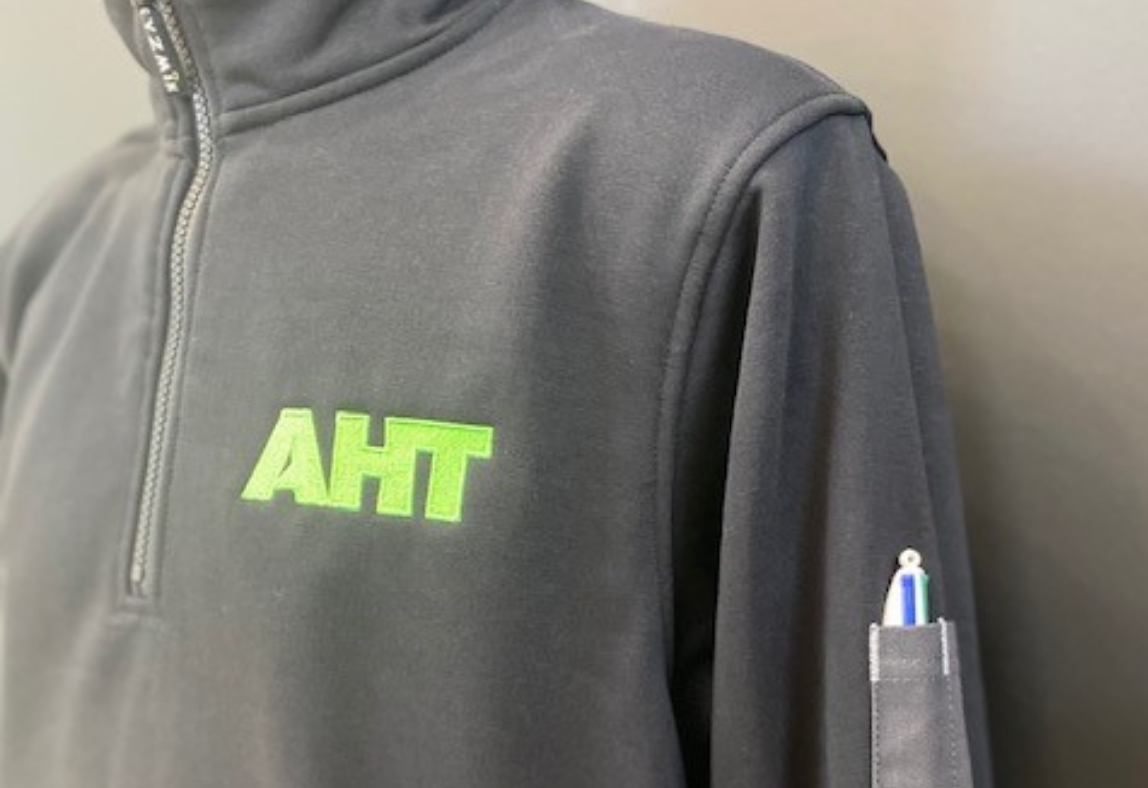 Green AHT logo embroidered onto a jumper with a pen pocket