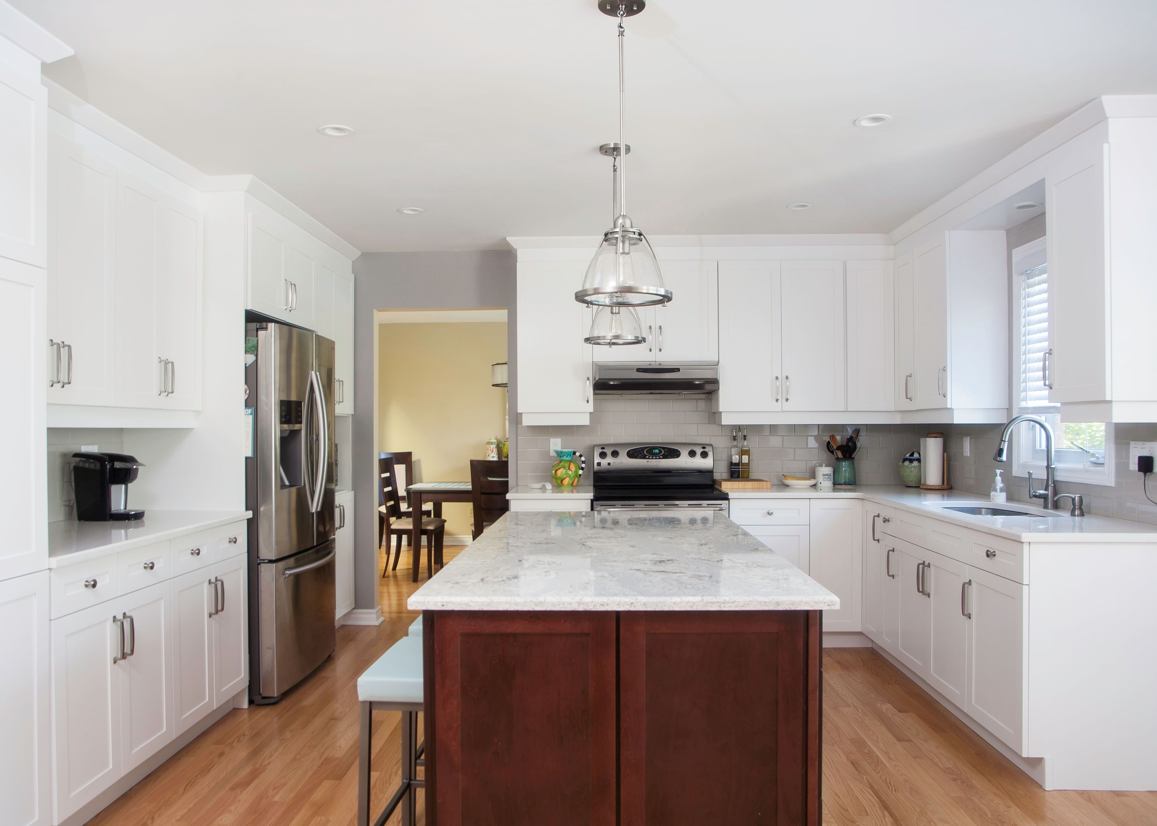 Beautfiul Kitchen Renovation by Family Home Improvements The redesigned kitchen feature stainless steel appliances, white cupboards, and island counter with marble countertop, dark wood base and seating, as well as plenty of space to move around.