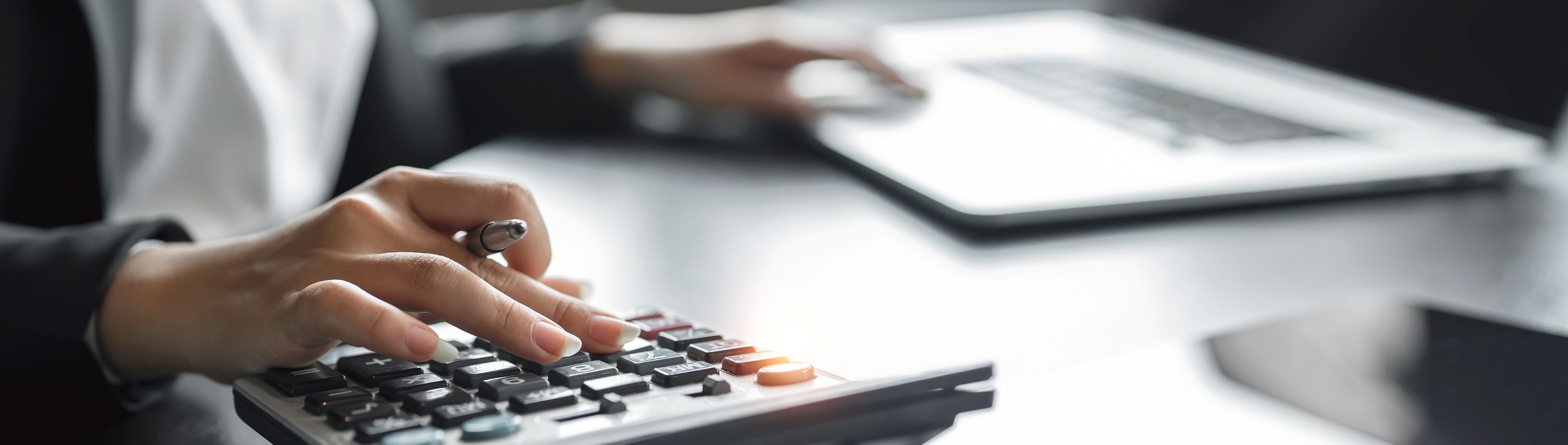 A woman working on financial reports at a desk, using a calculator, pen and laptop A woman working on financial reports at a desk, using a calculator, pen and laptop