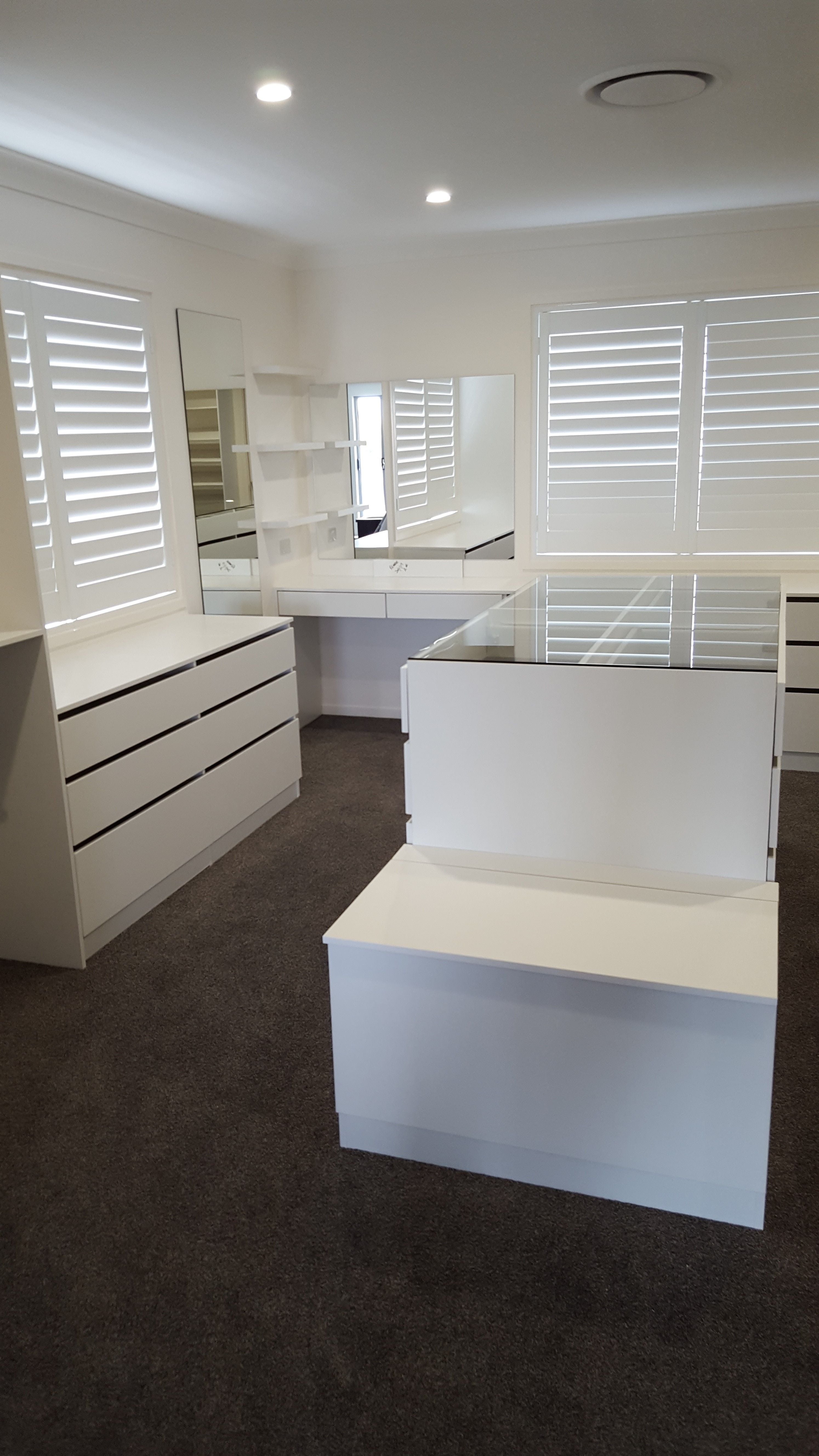 WIR using White HMR Melamine, centre island with 6mm toughened clear glass top. No backing. Open drawer fronts and white 32mm diameter hanging rail. Built in makeup station with floating shelves & mirror