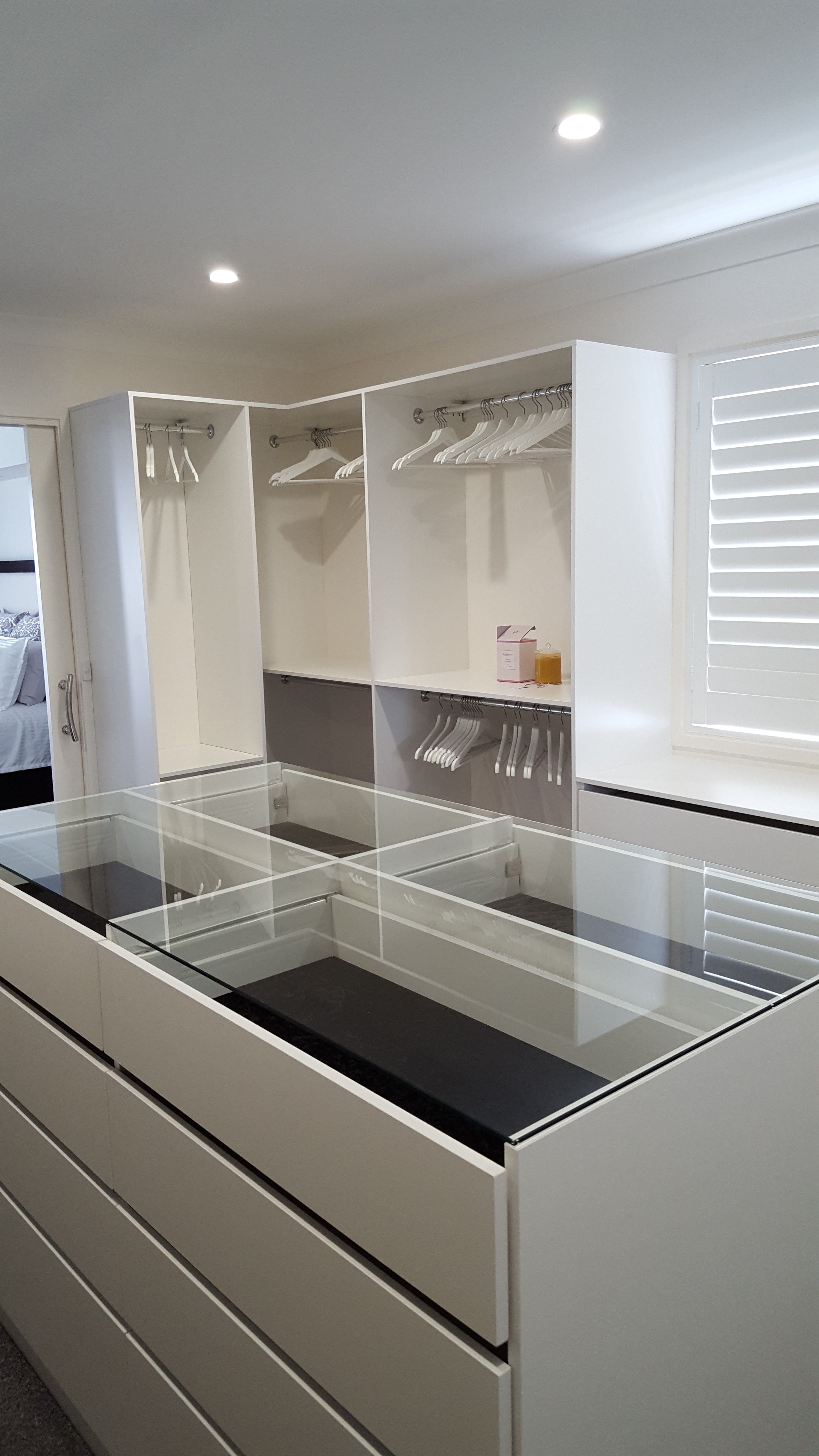 WIR using White HMR Melamine, centre island with 6mm toughened clear glass top. No backing. Open drawer fronts and white 32mm diameter hanging rail