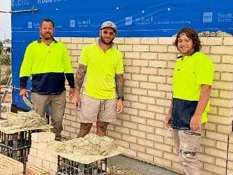 Photo of Jackson Doudle, Daniel Spears and Sean Wakka standing in front of partially constructed brick wall