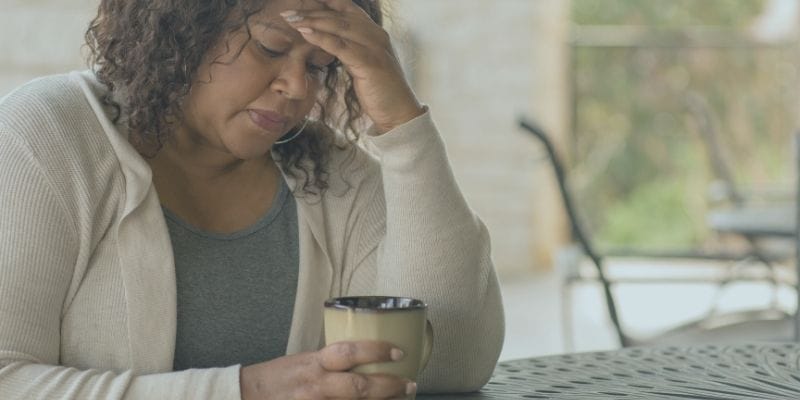 Woman resting her head in her hand and looking down into a cup of tea or coffee