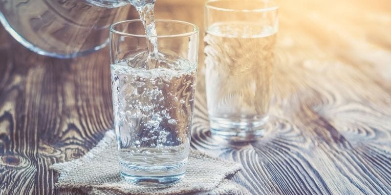 Two glasses being filled with water on a wooden table in the summer sun.