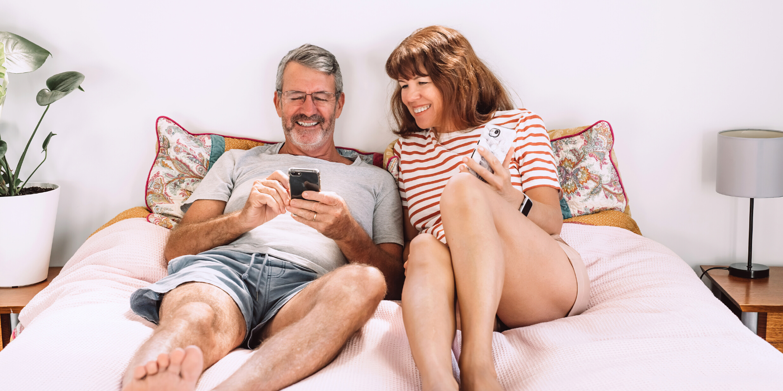 Man and woman over 50 in bed next to each other smiling and chatting