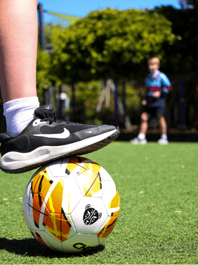 Developing Skills Through Sport and Play Student with foot on soccer ball on school courts during physical education lesson